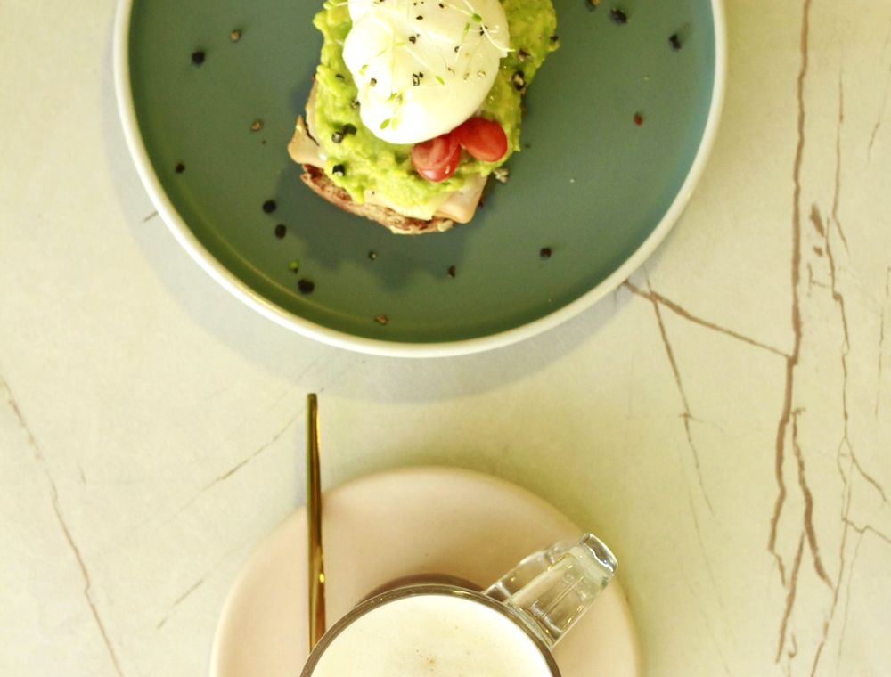 Tostada de aguacate y huevo servida con un café con leche
